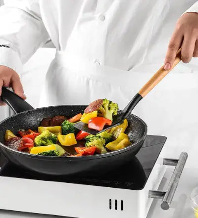 Chef stir-frying vegetables in a silicon kitchen utensil with bambus handle on induction cooktop